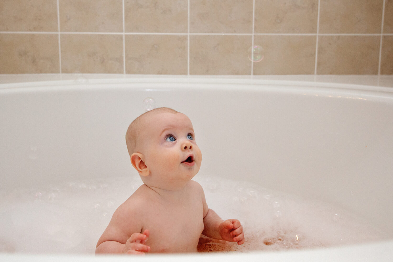 Surprised and excited baby boy in the tub looking at bubbles