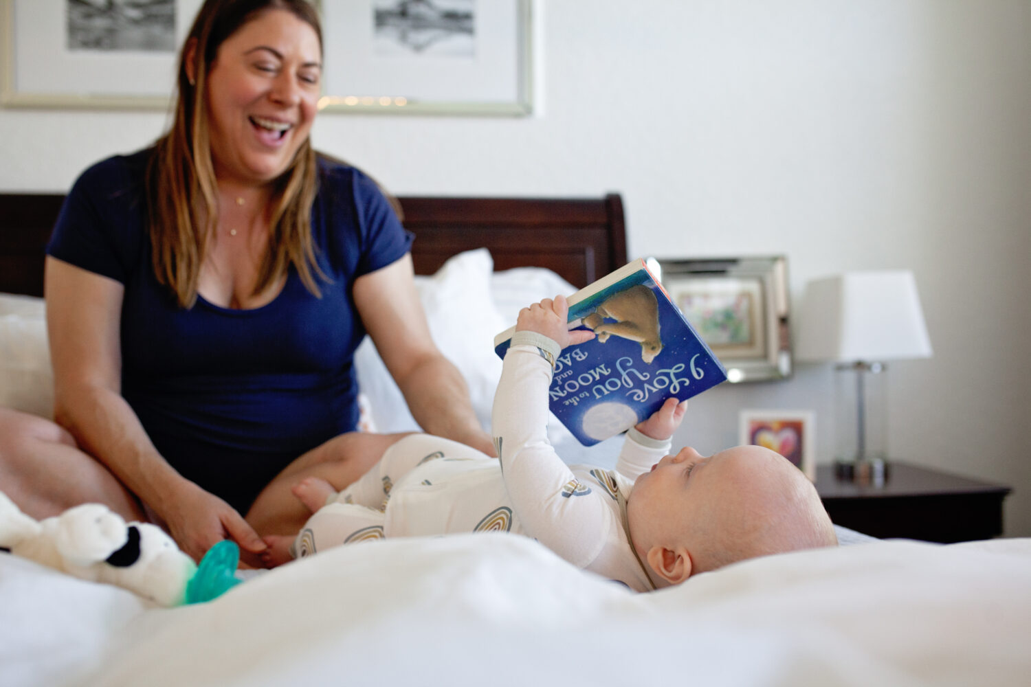 Baby examining book while mom laughs