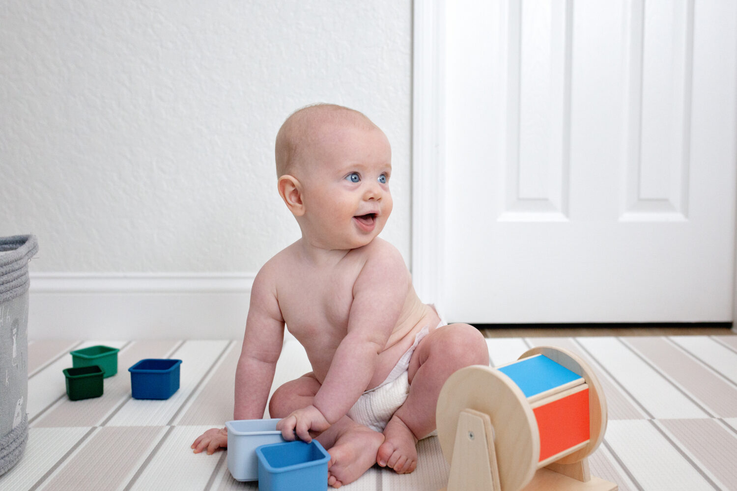 Laughing blue eyed baby sitting and playing with wooden toys