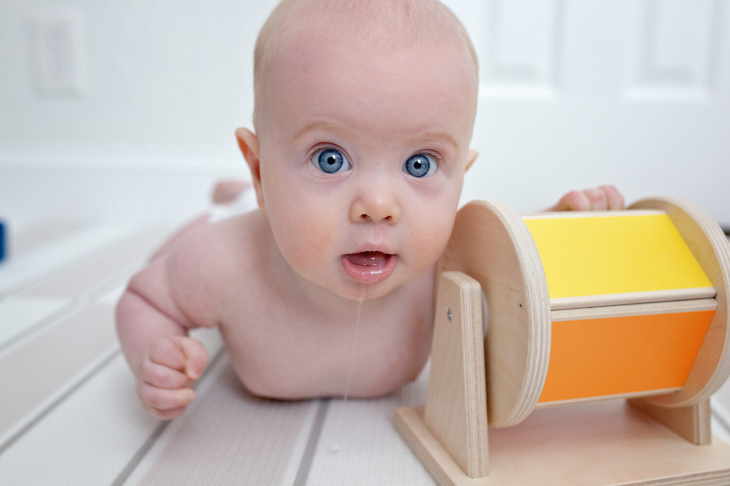 Baby doing tummy time with wooden toy.