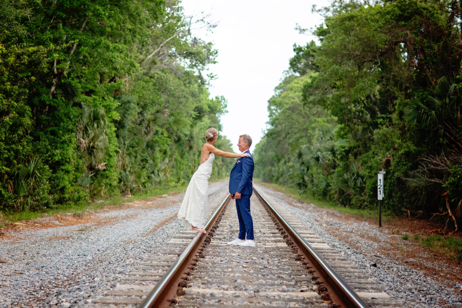 a bride leaning on her groom on a train track and looking away
