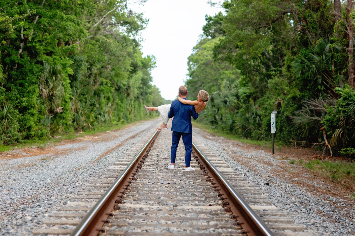 a groom carrying a bride away on the train tracks
